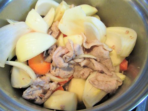 肉じゃがの作り方1。鍋に炒め油（分量外）を熱して豚肉を炒め、じゃがいも、にんじん、玉ねぎも加えて炒めます。